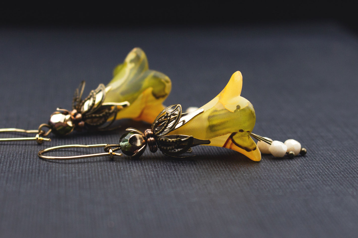 Seitliche Ansicht von Blütenohrringen in Creme, Gelb und Olivgrün mit goldfarbenen Glasperlen