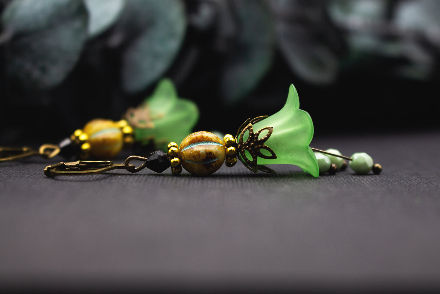 Grüne Ohrhänger mit Glasperlen in Ocker und Schwarz, filigraner Schmuck im botanischen Stil.