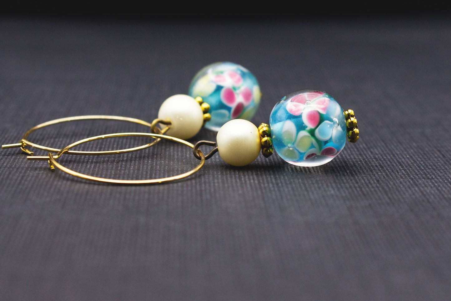 Detailaufnahme goldfarbene Creolen mit türkisfarbenen Glasperlen, Blumenmuster und cremeweißer Perle