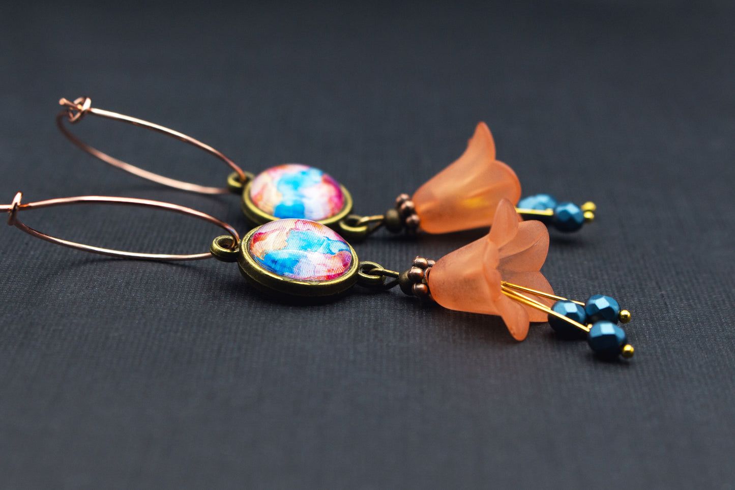 Detailaufnahme von Creolen mit orangefarbenen Acrylblüten und schimmerndem Cabochon in Petrol