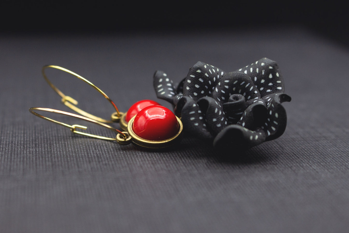 Detailaufnahme von schwarzen Blütenohrringen mit weißen Punkten und roter Glasperle