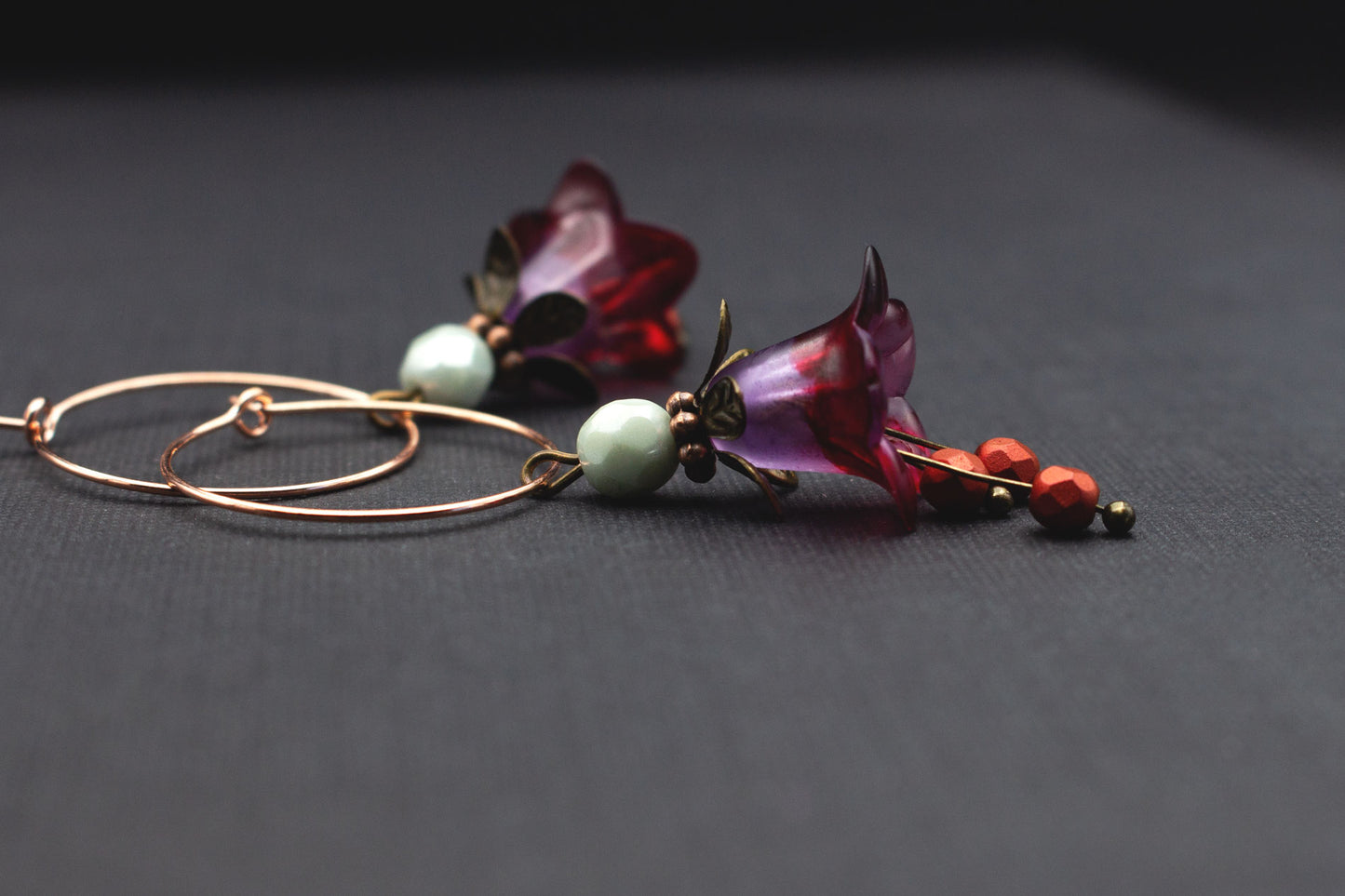 Detailansicht Roségold-Creolen mit lila-roten Acrylblüten und Glasperlen