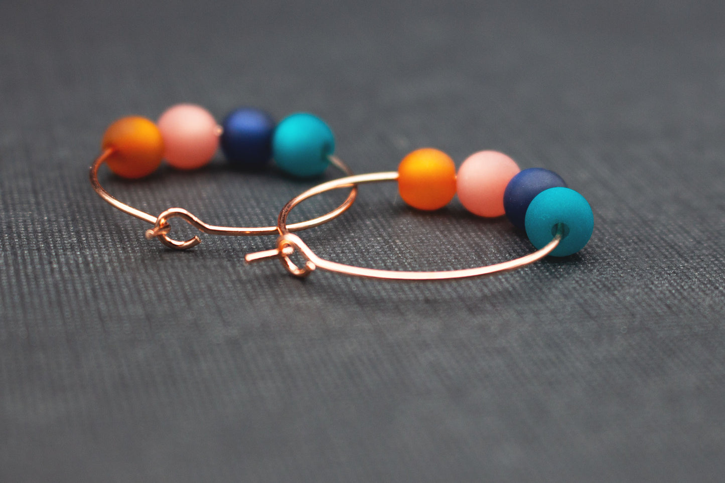 Detailaufnahme von Roségold Creolen mit Polarisperlen in Türkis, Dunkelblau und Rosa
