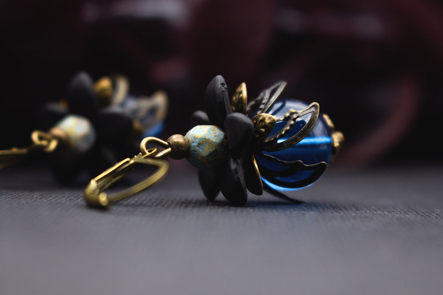 Blütenohrringe in Blau und Schwarz mit transparenter Glasperle, Acrylblüte und Bronze – tiefblauer Vintage-Schmuck für elegante Outfits.