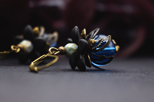 Blütenohrringe in Blau und Schwarz mit transparenter Glasperle, Acrylblüte und Bronze – tiefblauer Vintage-Schmuck für elegante Outfits.