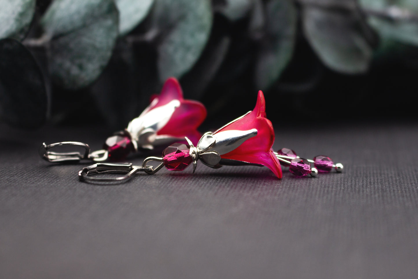 Nahaufnahme handbemalter Blütenohrringe mit fuchsiafarbenen Blüten und silberfarbenem Metall