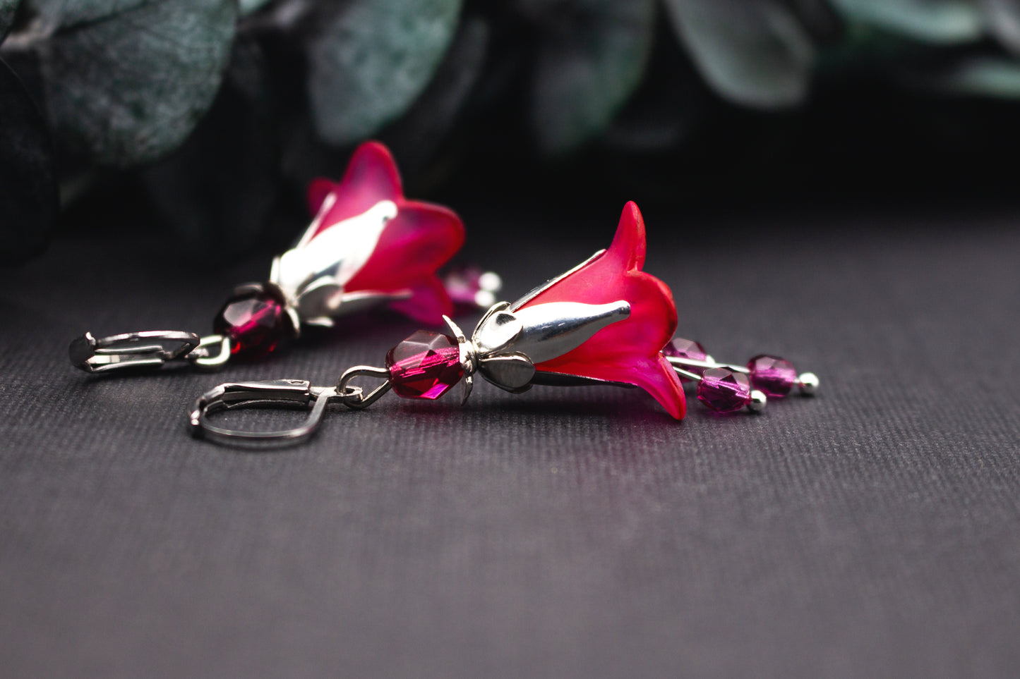 Handbemalte Blütenohrringe in Fuchsia Pink mit silberfarbenen Metallelementen auf dunklem Hintergrund fotografiert