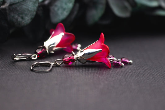 Handbemalte Blütenohrringe in Fuchsia Pink mit silberfarbenen Metallelementen auf dunklem Hintergrund fotografiert