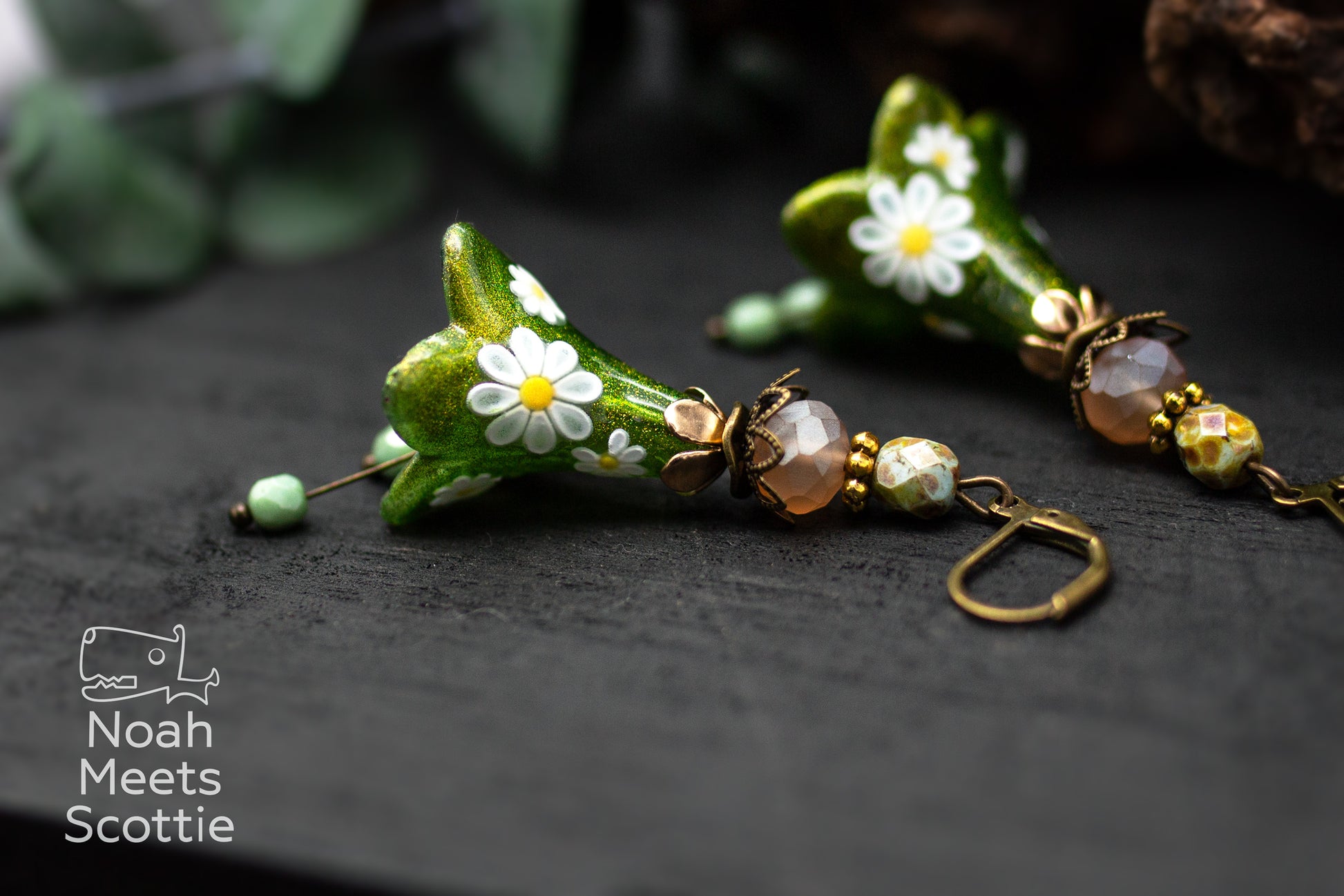 Florale Ohrringe mit großen grünen Blüten, bronzefarbenen Fassungen und abgestimmten Glasperlen.