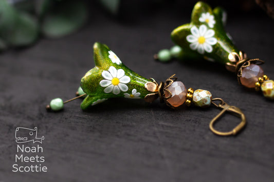 Handbemalte grüne Blütenohrringe mit kleinen weißen Margeriten, bronzefarbenen Metallelementen und Glasperlen.