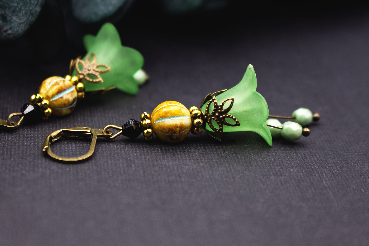 Detailaufnahme hellgrüner Blütenglocken-Ohrringe mit ockerner Glasperle und harmonischen Schmuckelementen.