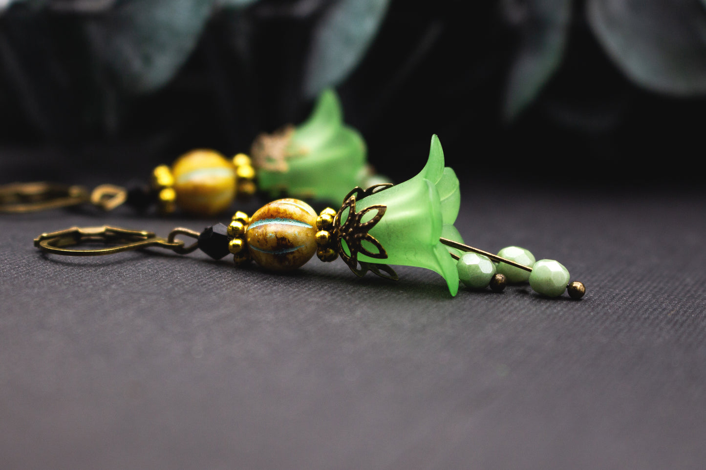 Hellgrüne Blütenohrringe mit ockerfarbener Glasperle und Antik-Bronze-Details, natürlicher floraler Ohrschmuck im warmen Farbspiel.