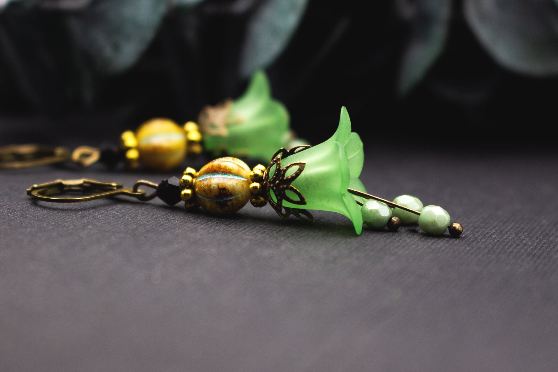 Hellgrüne Blütenohrringe mit ockerfarbener Glasperle und Antik-Bronze-Details, natürlicher floraler Ohrschmuck im warmen Farbspiel.