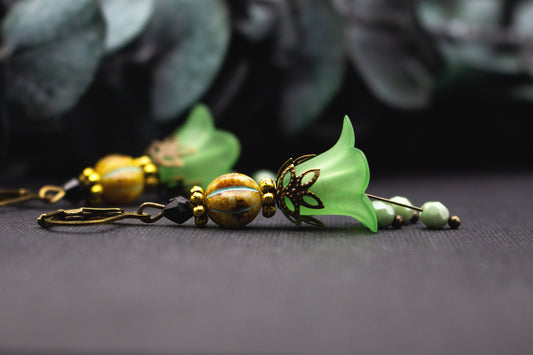 Hellgrüne Blütenohrringe mit ockerfarbener Glasperle und Antik-Bronze-Details, natürlicher floraler Ohrschmuck im warmen Farbspiel.