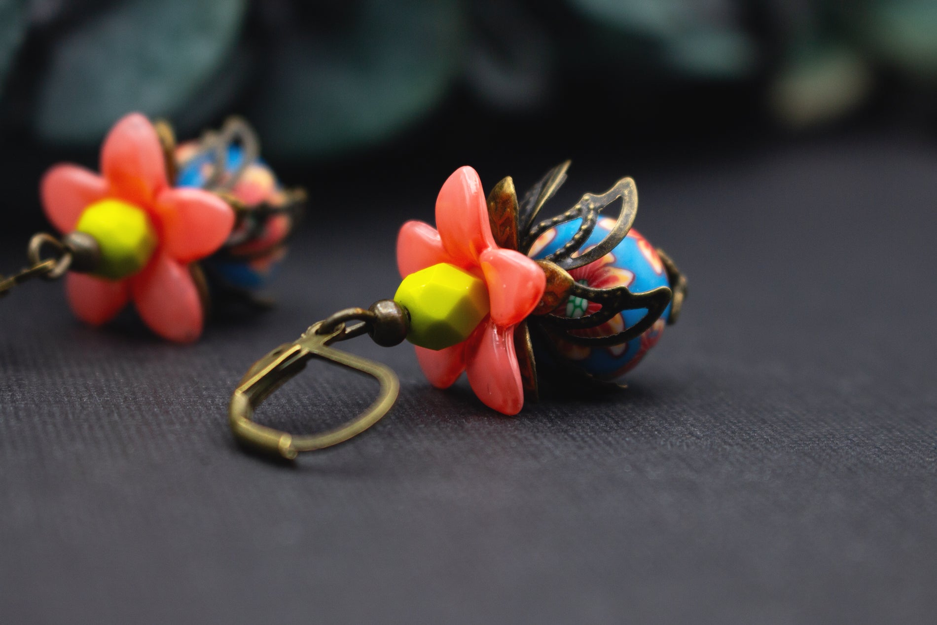 Nahaufnahme von lachsrosa Blütenohrringen mit gelber Perle und gemusterter blauer Glasperle, floraler Schmuck im Vintage-Stil.