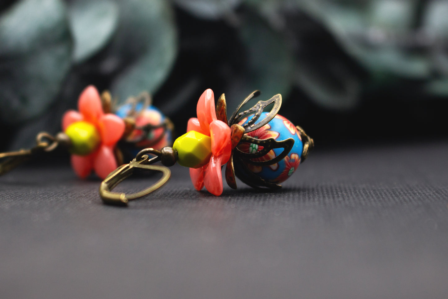 Blütenohrringe in Lachsrosa und Blau mit gelber Glasperle und floralen Mustern, detailreicher Ohrschmuck mit antik-bronzefarbenen Elementen.