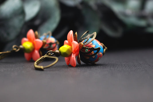 Blütenohrringe in Lachsrosa und Blau mit gelber Glasperle und floralen Mustern, detailreicher Ohrschmuck mit antik-bronzefarbenen Elementen.