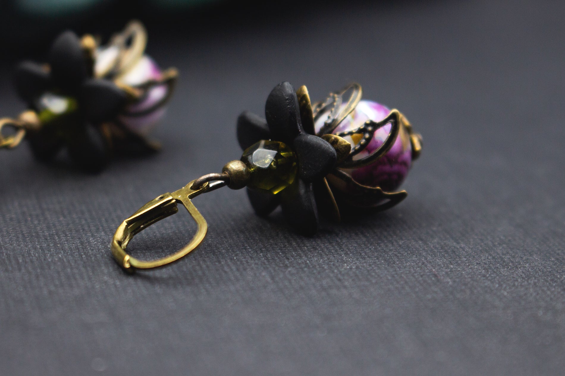 Marmorierte Lila-Glasperlenohrringe mit olivgrünem Akzent und schwarzen Blüten – kunstvoller floraler Ohrschmuck mit warmem Vintage-Charakter.