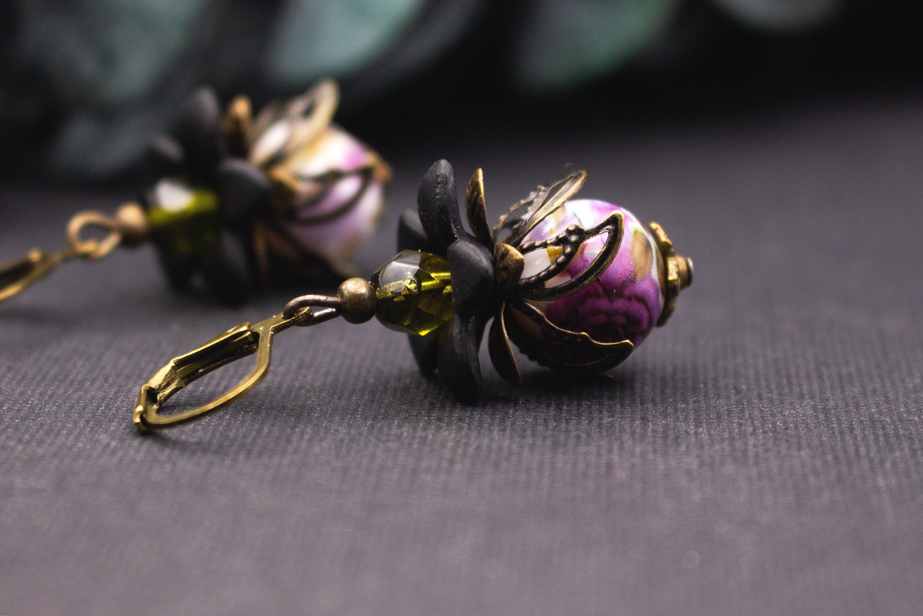 Florale Lila-Oliv Ohrhänger mit marmorierter Perle, dunklen Blüten und Bronzeelementen – eleganter Vintage-Schmuck im markanten Design.