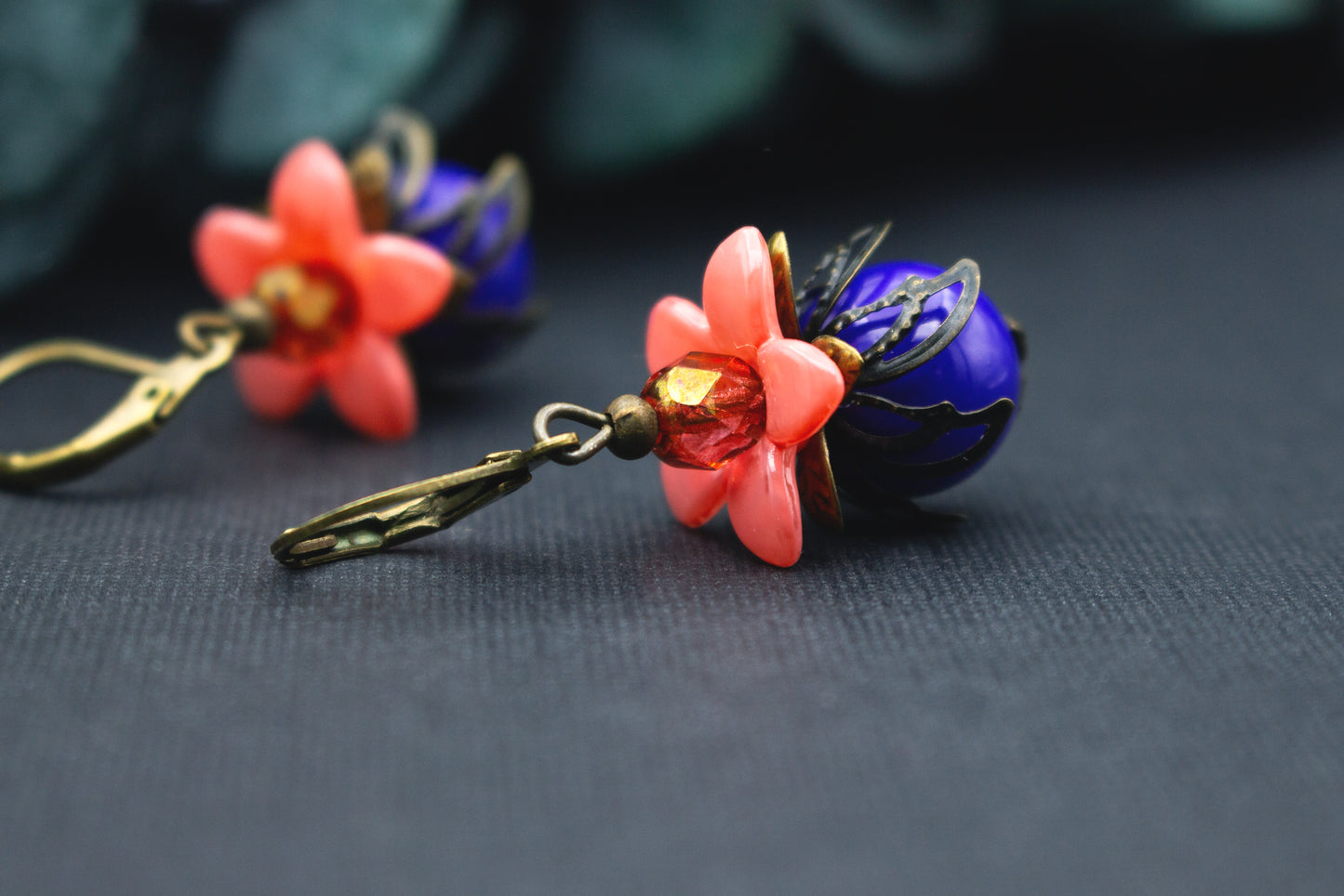 Orange-Blaue Blumenohrringe mit Acrylblüte, facettierter Glasperle und bronzenen Details – auffälliger floraler Ohrschmuck für moderne Outfits.