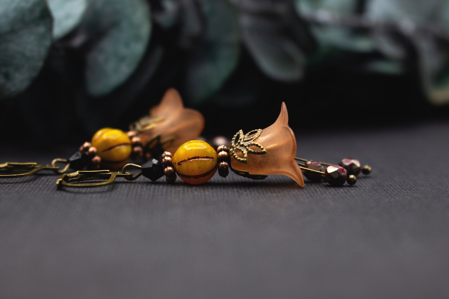 Orangefarbene Blütenohrringe mit gemaserter Gelbperle und schwarzen Akzenten – leichte Ohrhänger im warmen Farbkontrast.