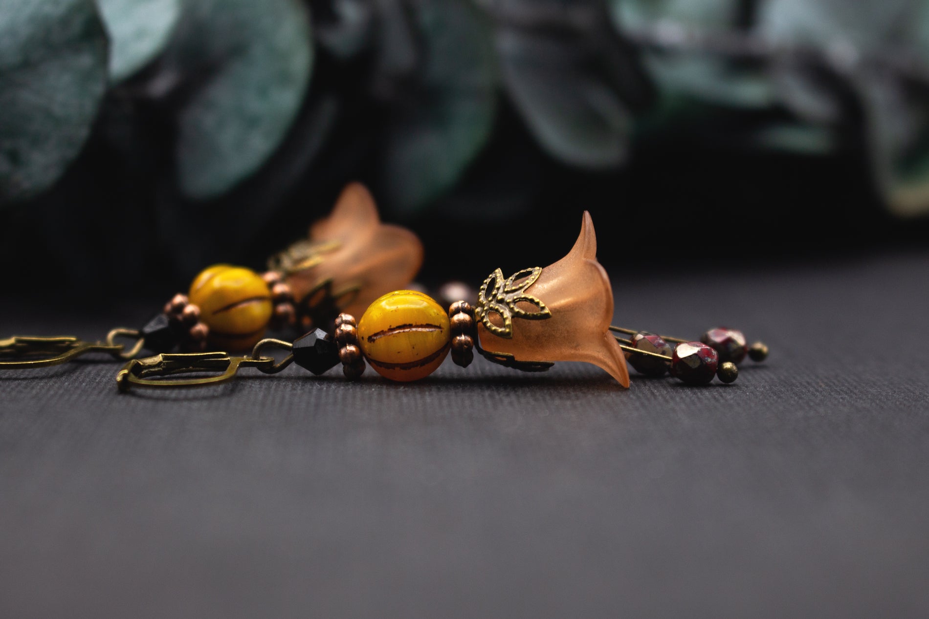 Orangefarbene Blütenohrringe mit gemaserter Gelbperle und schwarzen Akzenten – leichte Ohrhänger im warmen Farbkontrast.