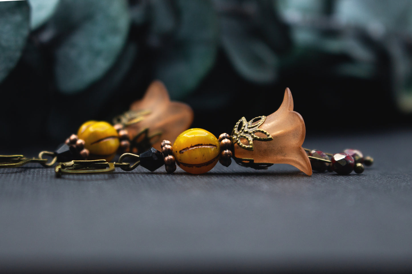 Orange-Gelbe Blütenohrringe mit warmer Glasperle, bronzenen Elementen und schwarzem Akzent – leichter Schmuck im natürlichen, herbstlichen Farbspiel.