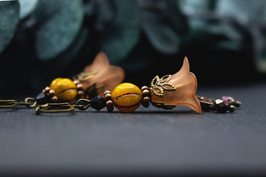 Orange-Gelbe Blütenohrringe mit warmer Glasperle, bronzenen Elementen und schwarzem Akzent – leichter Schmuck im natürlichen, herbstlichen Farbspiel.