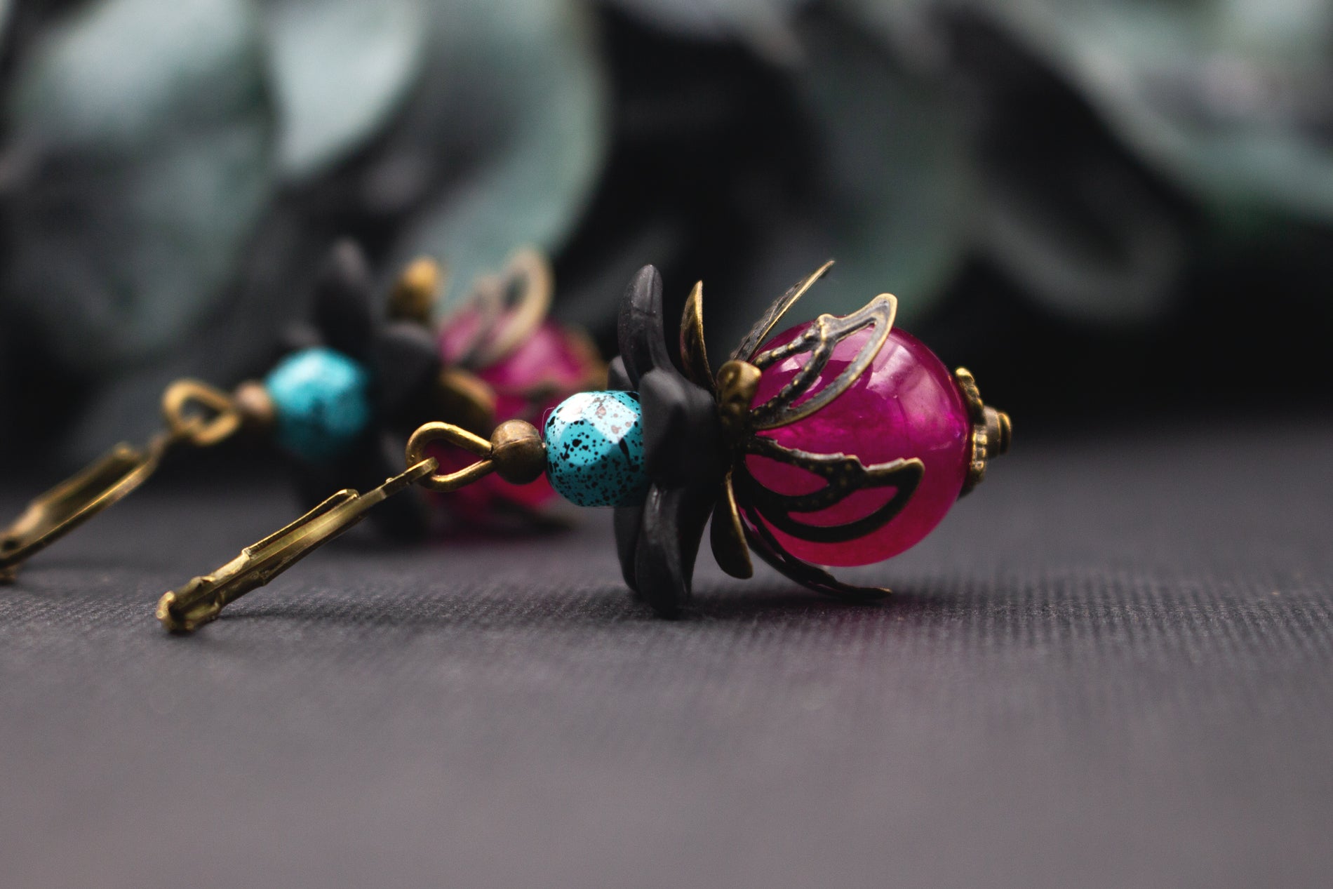 Pinke Glasperlenohrringe mit türkis gesprenkelter Akzentperle, Bronze-Elementen und schwarzen Blüten – kunstvoller Ohrschmuck im floralen Vintage-Stil.