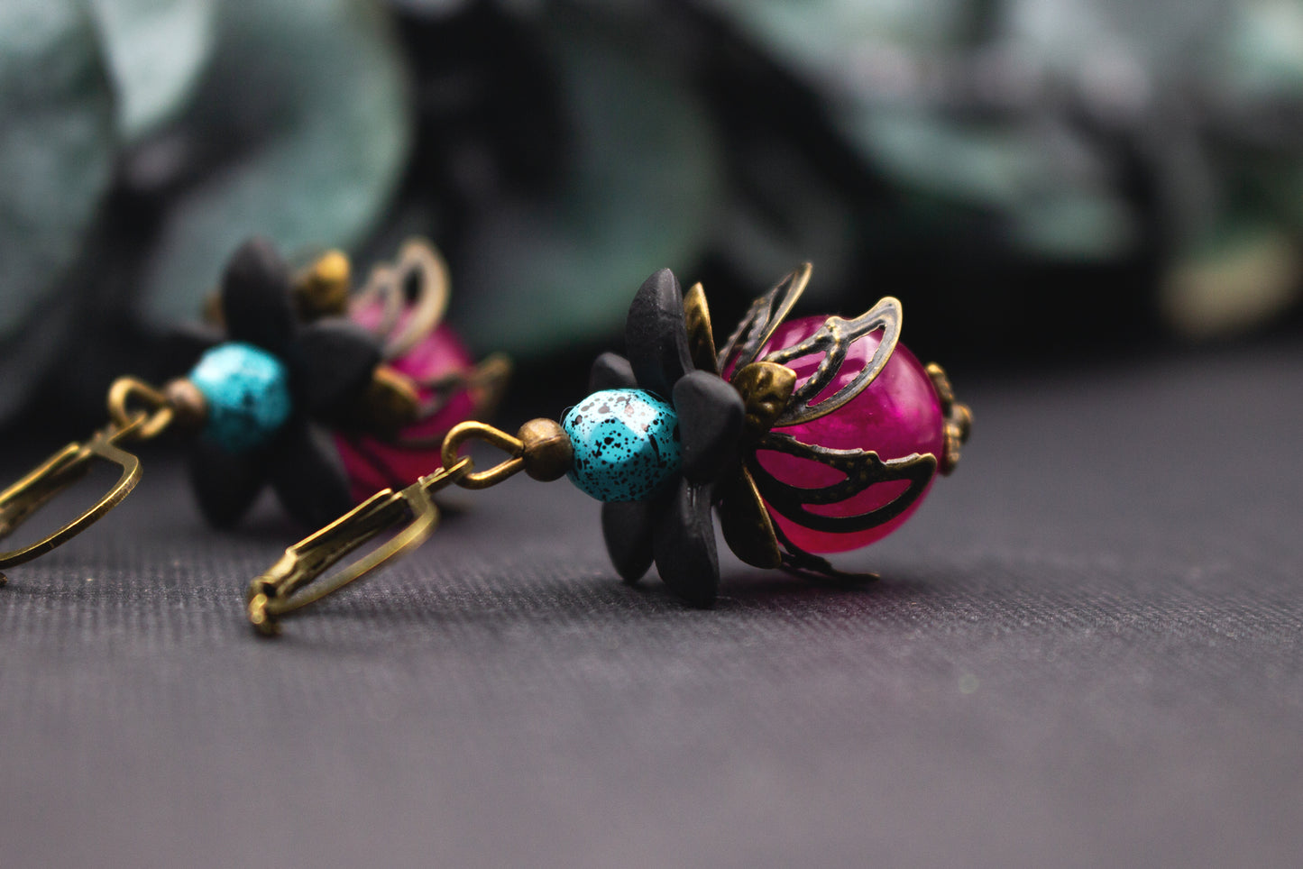 Vintage-Ohrringe in Pink und Türkis mit schwarzen Acrylblüten und bronzenen Metallblättern – detailreicher Schmuck mit leuchtenden Farben.