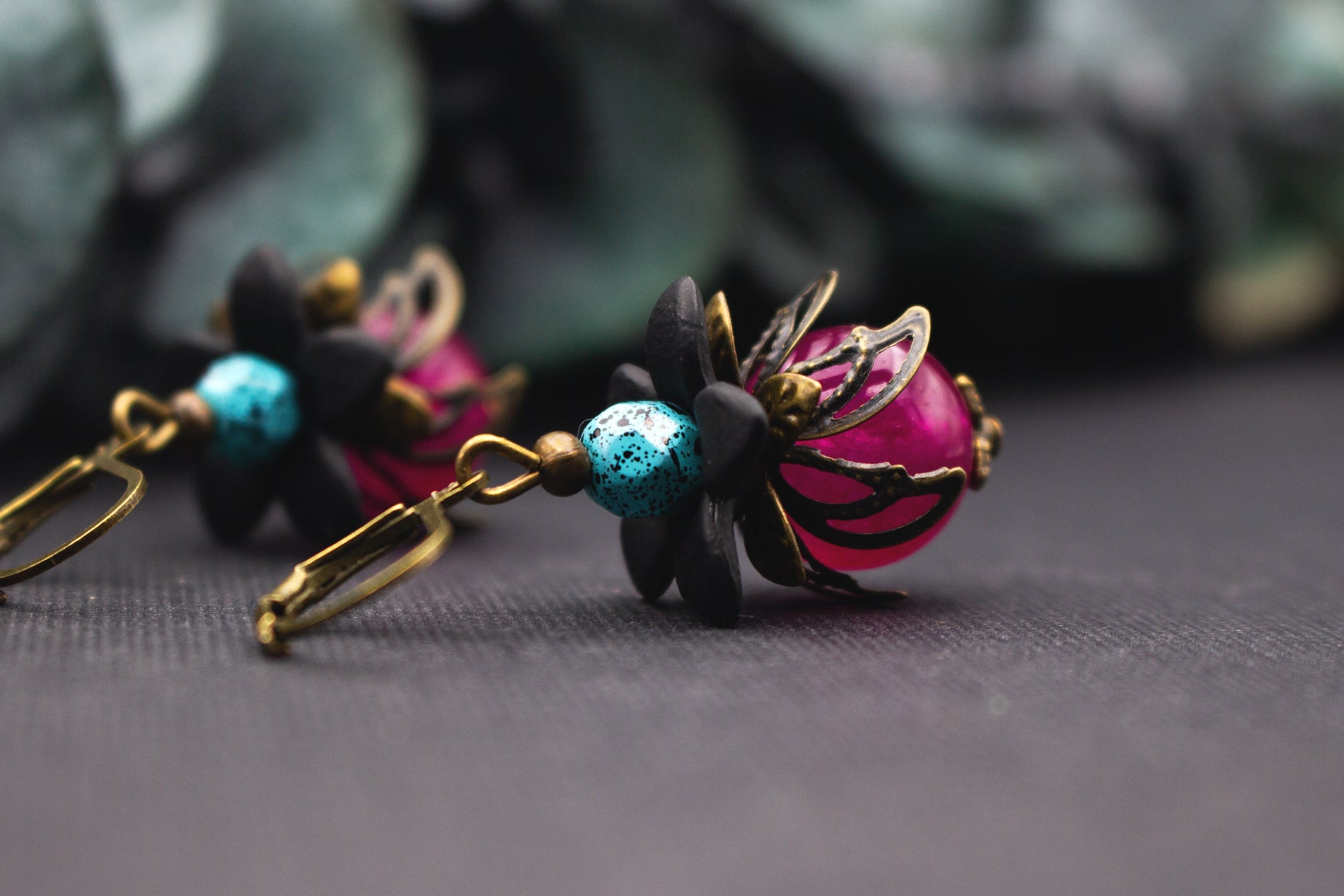 Vintage-Ohrringe in Pink und Türkis mit schwarzen Acrylblüten und bronzenen Metallblättern – detailreicher Schmuck mit leuchtenden Farben.