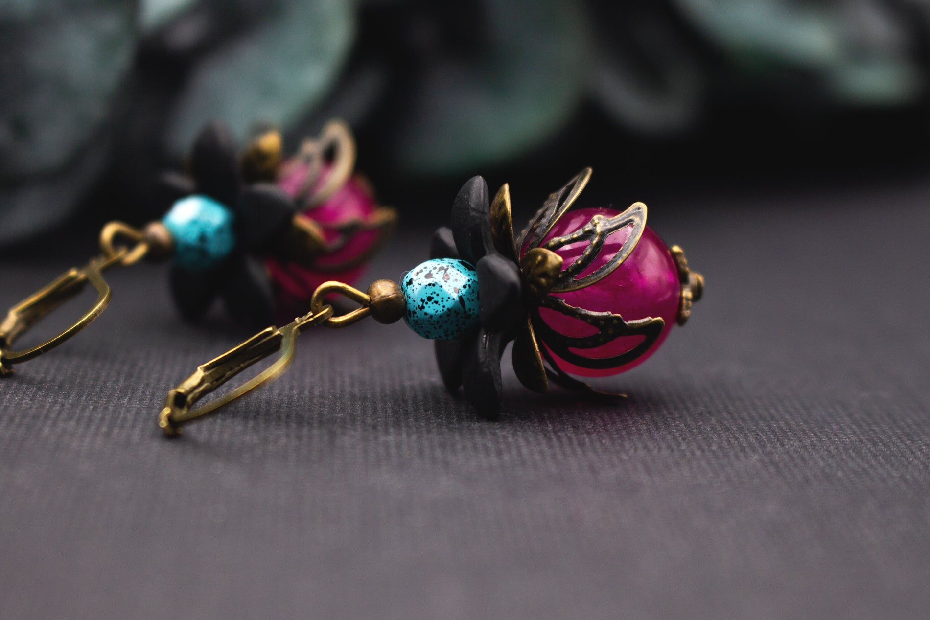 Florale Pink-Türkis Blütenohrringe mit glänzender Glasperle, schwarzen Acrylblüten und bronzenen Metallkappen – kontrastreicher Vintage-Schmuck mit kräftigen Farben.