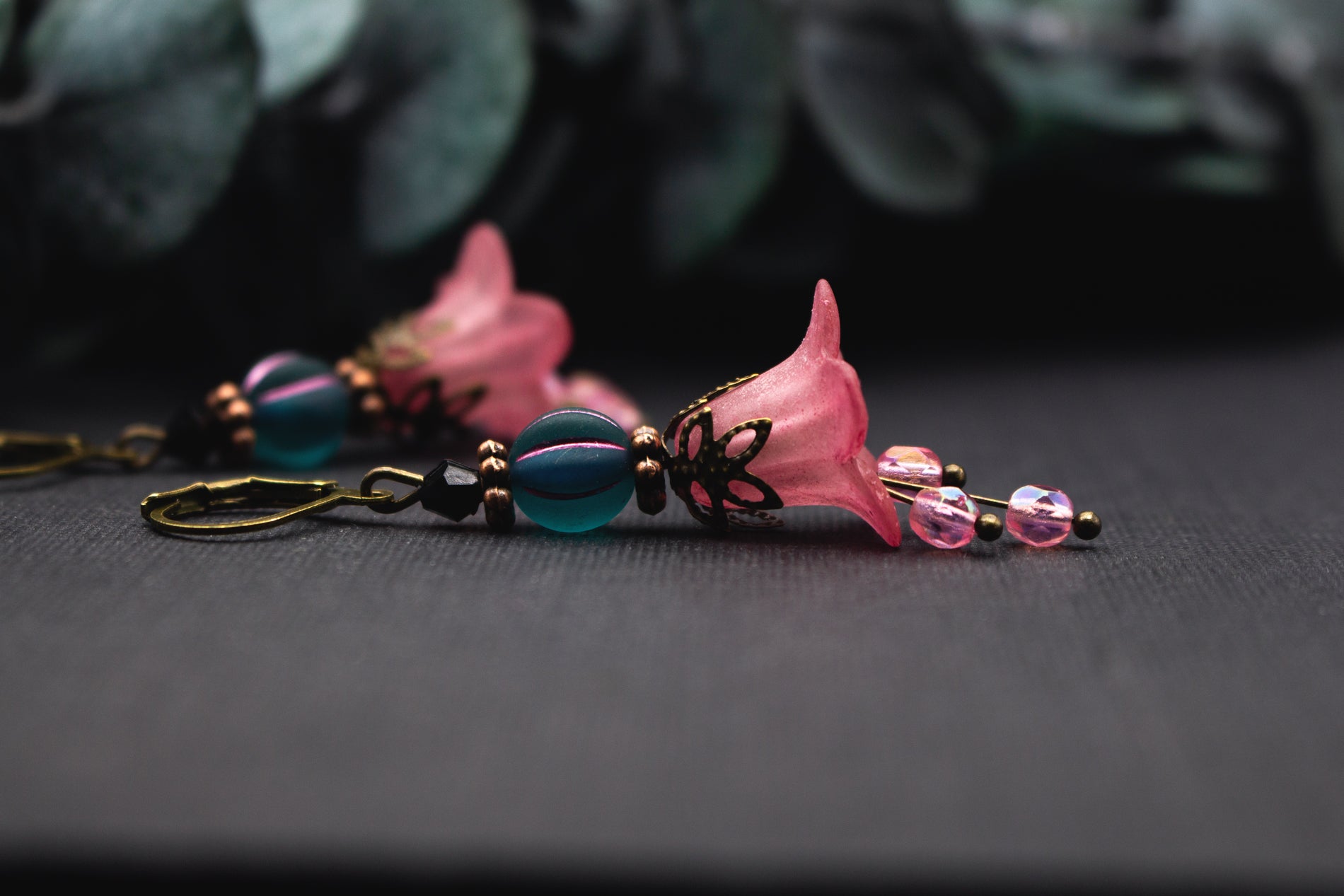 Ohrhänger mit rosa Blütenglocke, petrolfarbener Perle und schimmernden Glasakzenten – zartes Design im harmonischen Farbspiel.