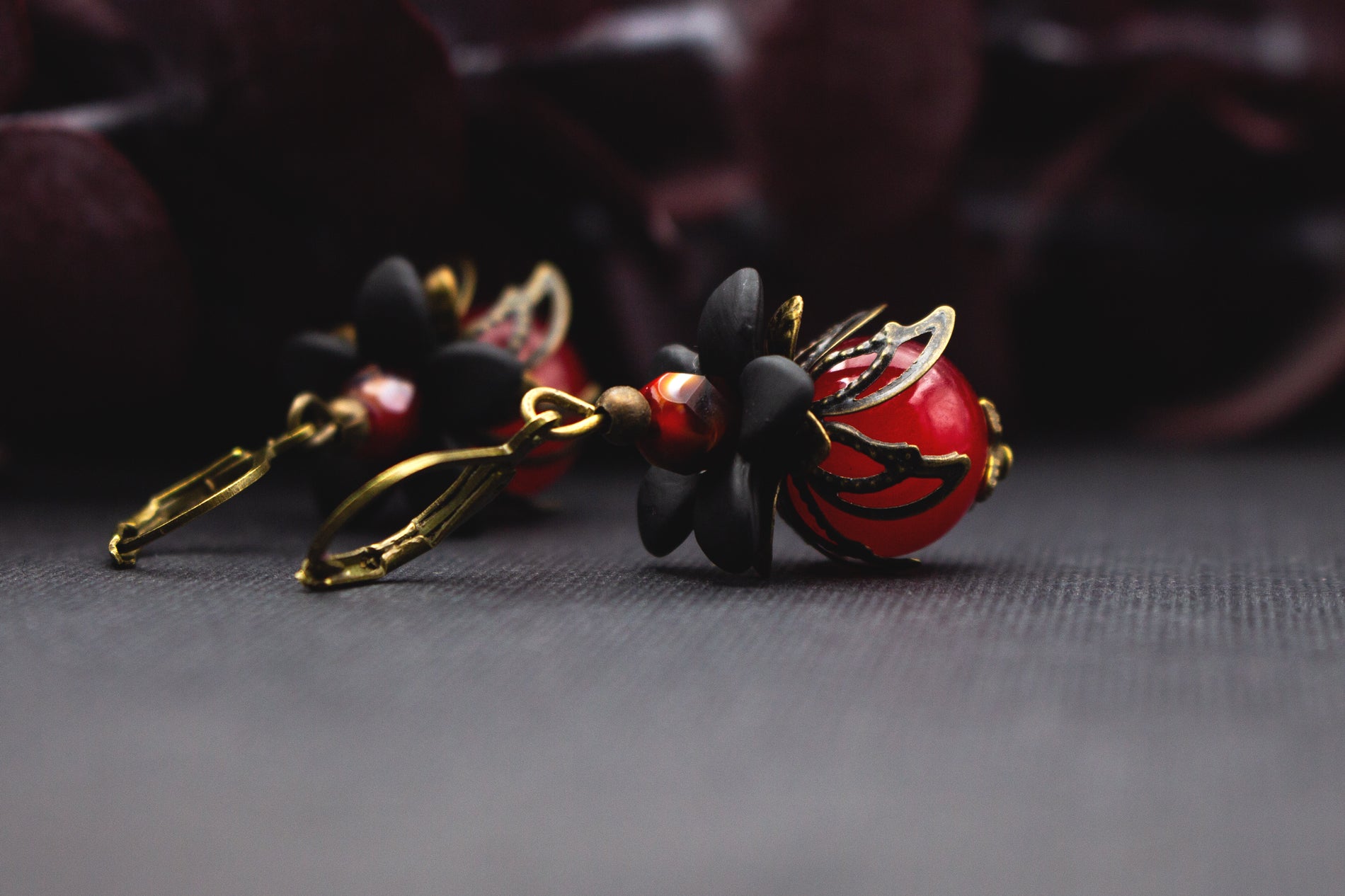 Romantische Blütenohrringe mit roter Glasperle, schwarzer Blüte und bronzefarbenem Metall – stilvoller Schmuck mit warmer Farbwirkung.