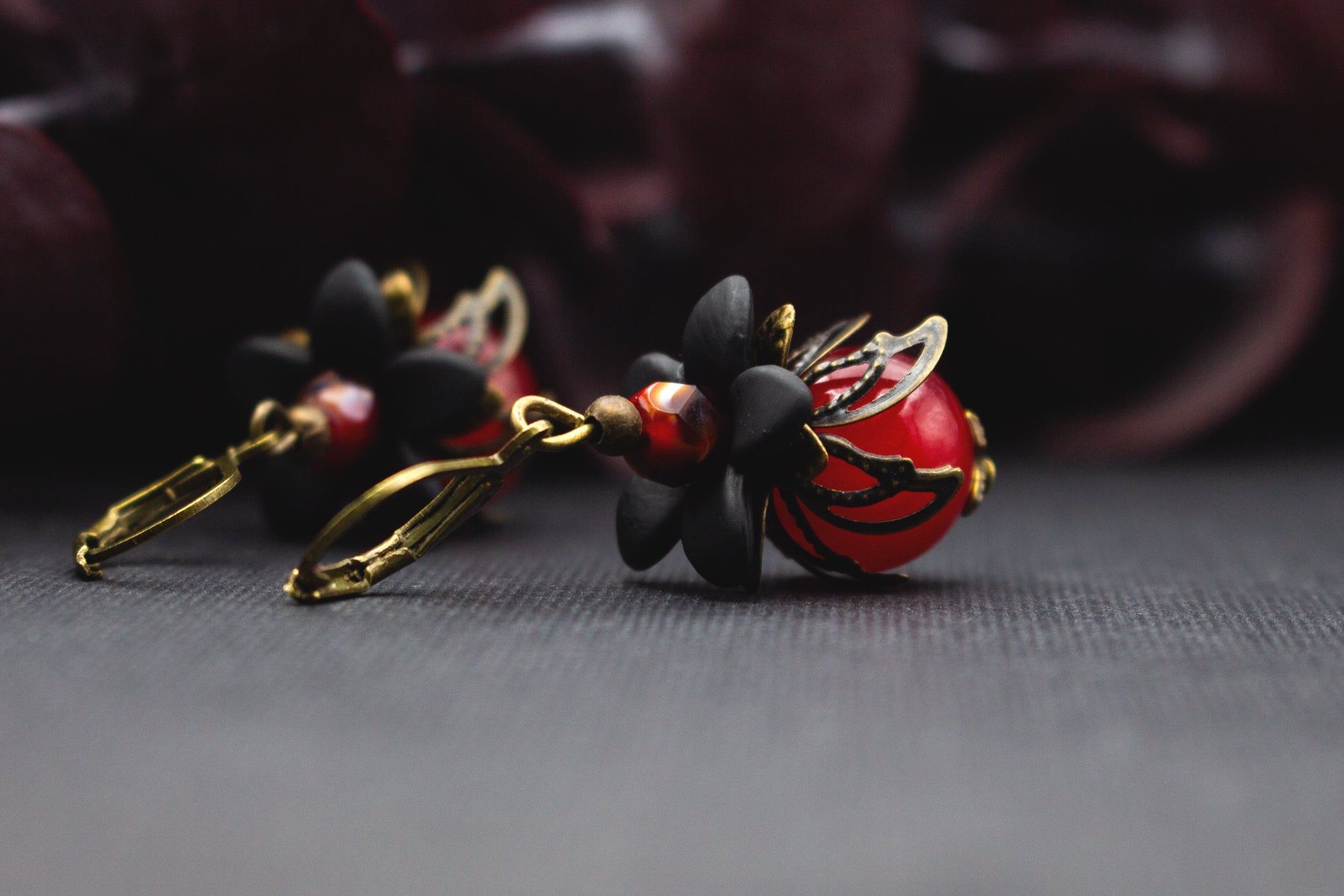 Blütenohrringe in Rot und Schwarz mit glänzender Glasperle und bronzefarbenen Metallblüten – romantischer Vintage-Schmuck für besondere Outfits.
