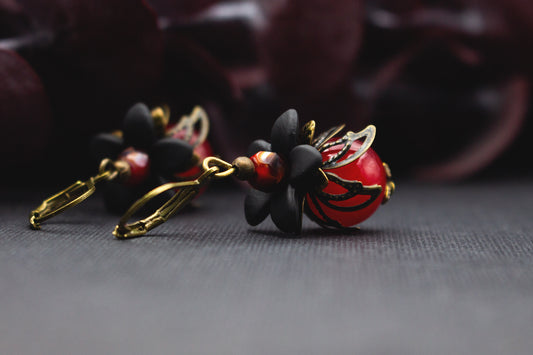 Blütenohrringe in Rot und Schwarz mit glänzender Glasperle und bronzefarbenen Metallblüten – romantischer Vintage-Schmuck für besondere Outfits.