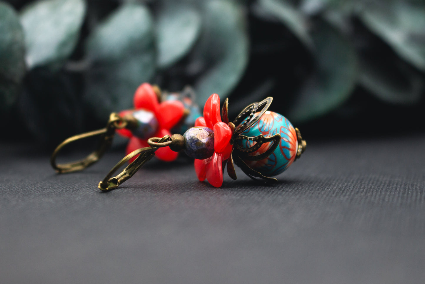 Rot-Türkis Blumenohrringe mit Acrylblüte, gemusterter Glasperle und bronzener Blütenkappe – lebendiger, kunstvoller Ohrschmuck.