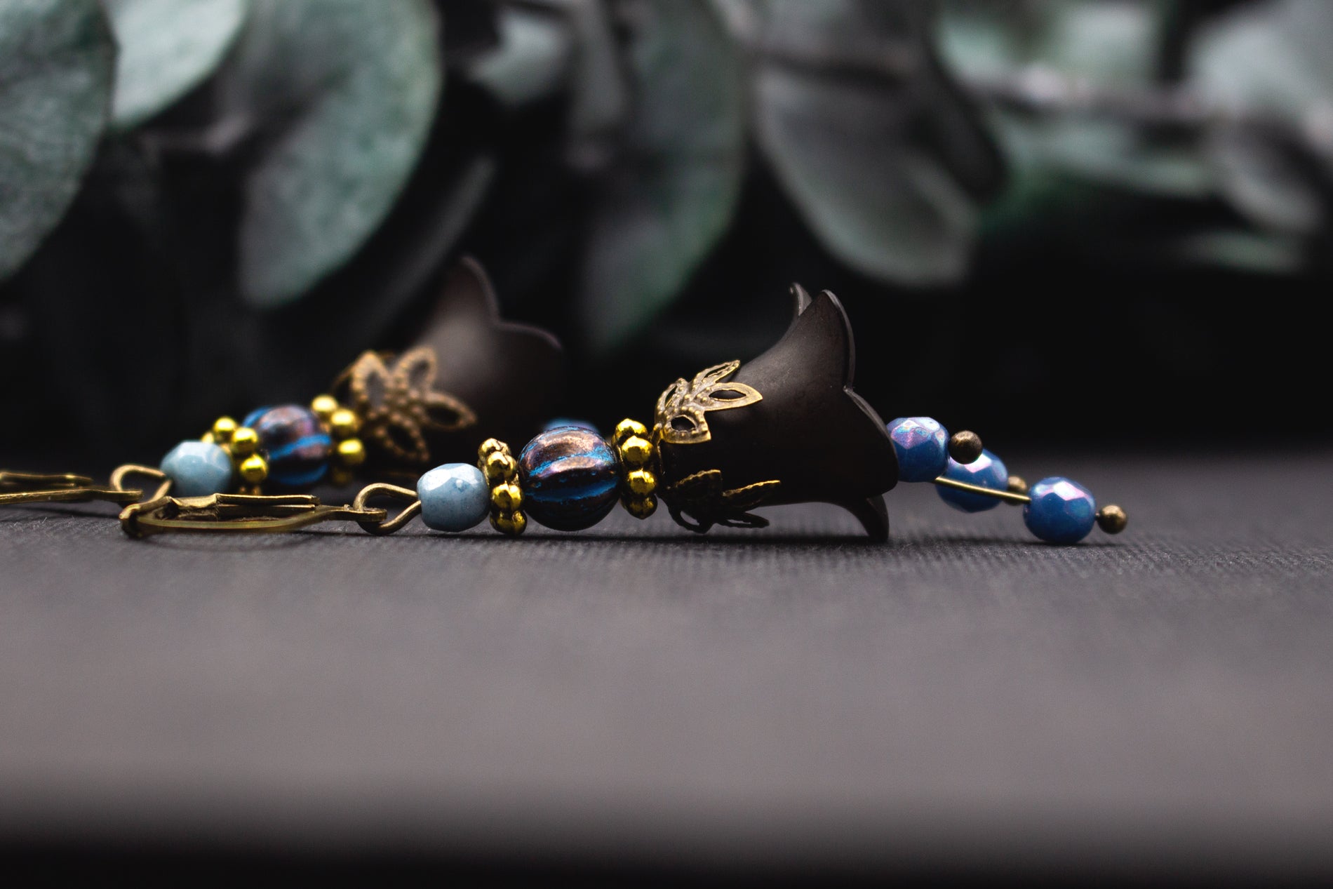 Schwarze Blütenohrringe mit blauen facettierten Perlen und goldfarbenen Details im Vintage-Stil