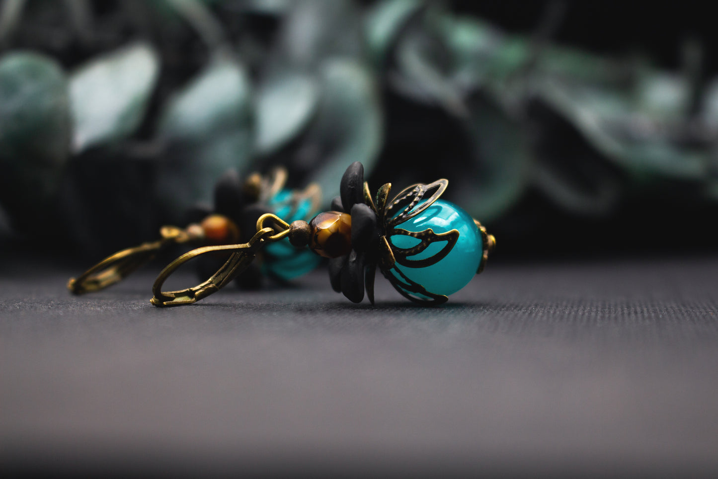 Türkis-Schwarz Blütenohrringe mit glänzender Glasperle und bronzenen Blütenelementen – mystischer Vintage-Ohrschmuck mit kraftvoller Farbwirkung und floralen Details.