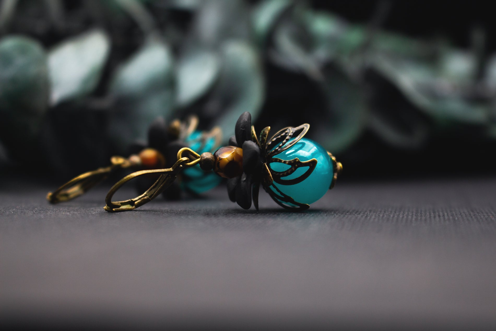 Türkis-Schwarz Blütenohrringe mit glänzender Glasperle und bronzenen Blütenelementen – mystischer Vintage-Ohrschmuck mit kraftvoller Farbwirkung und floralen Details.
