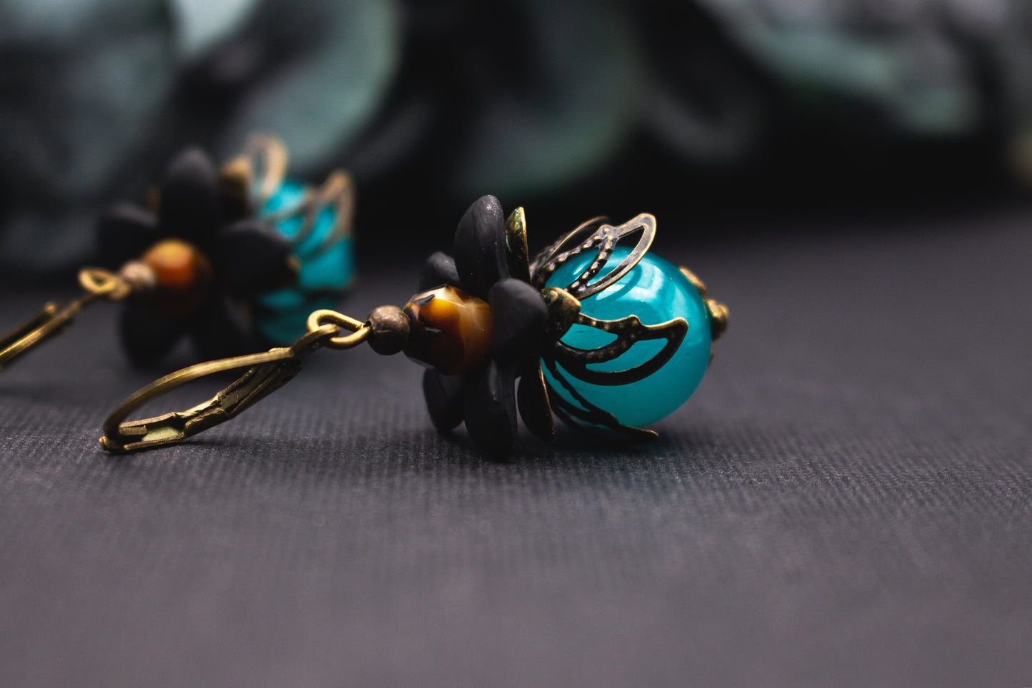 Ohrschmuck Türkis Schwarz mit glänzender Glasperle und fein gearbeiteter Metallblüte – eleganter floraler Schmuck mit Tiefe.