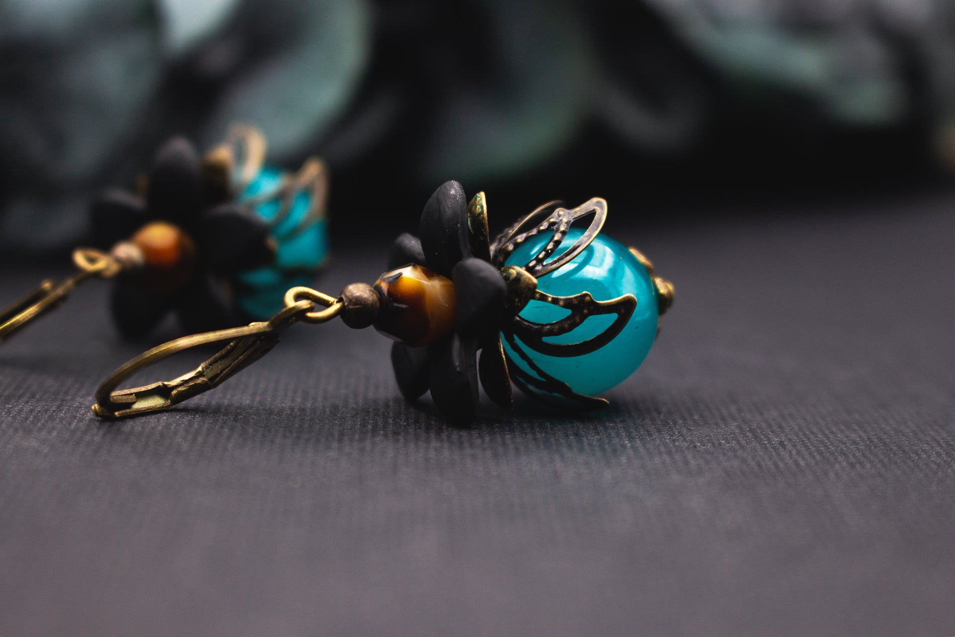 Ohrschmuck Türkis Schwarz mit glänzender Glasperle und fein gearbeiteter Metallblüte – eleganter floraler Schmuck mit Tiefe.