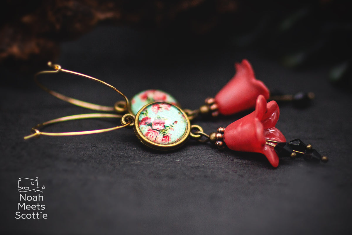 Rote Blütenohrringe mit glockenförmigen Blumenanhängern, schwarzen facettierten Perlen und bronzefarbenen Details.