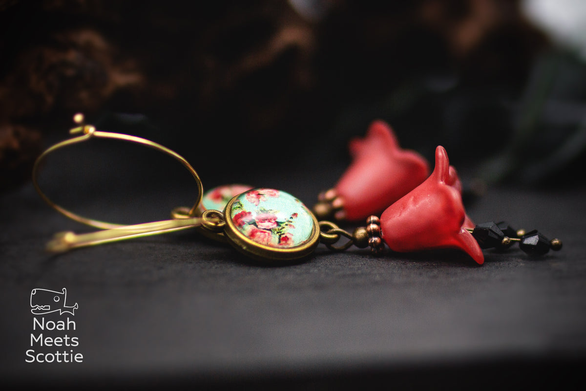 Goldfarbene Blumen Creolen mit roten Glockenblüten, hellblauem Cabochon mit Rosenmuster und schwarzen facettierten Perlen.
