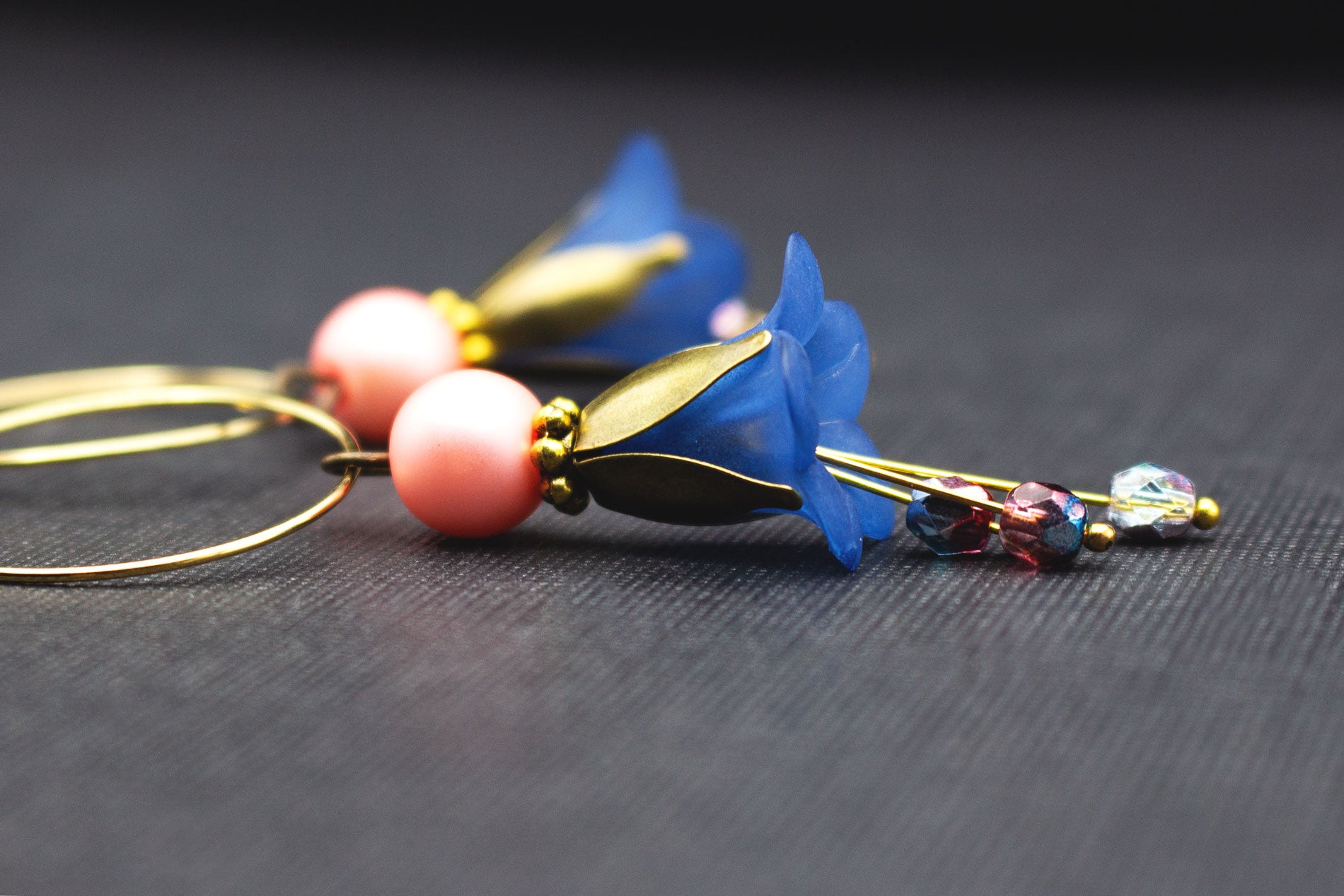 Detailaufnahme von Creolen in Gold mit dunkelblauen Blüten und rosa Glasperlen