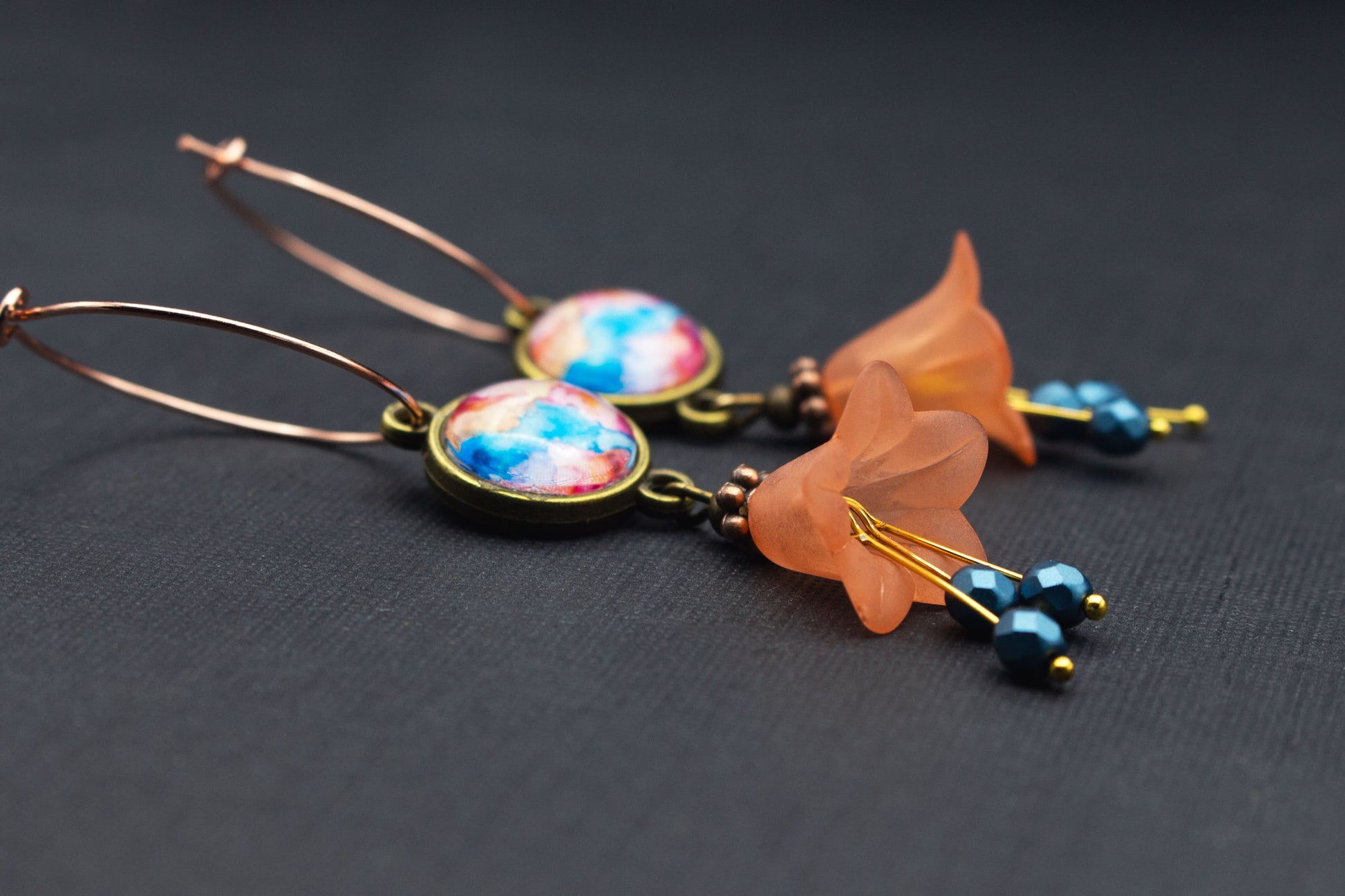 Seitenansicht von Creolen in Roségold mit orangefarbenen Acrylblüten und blauem Cabochon