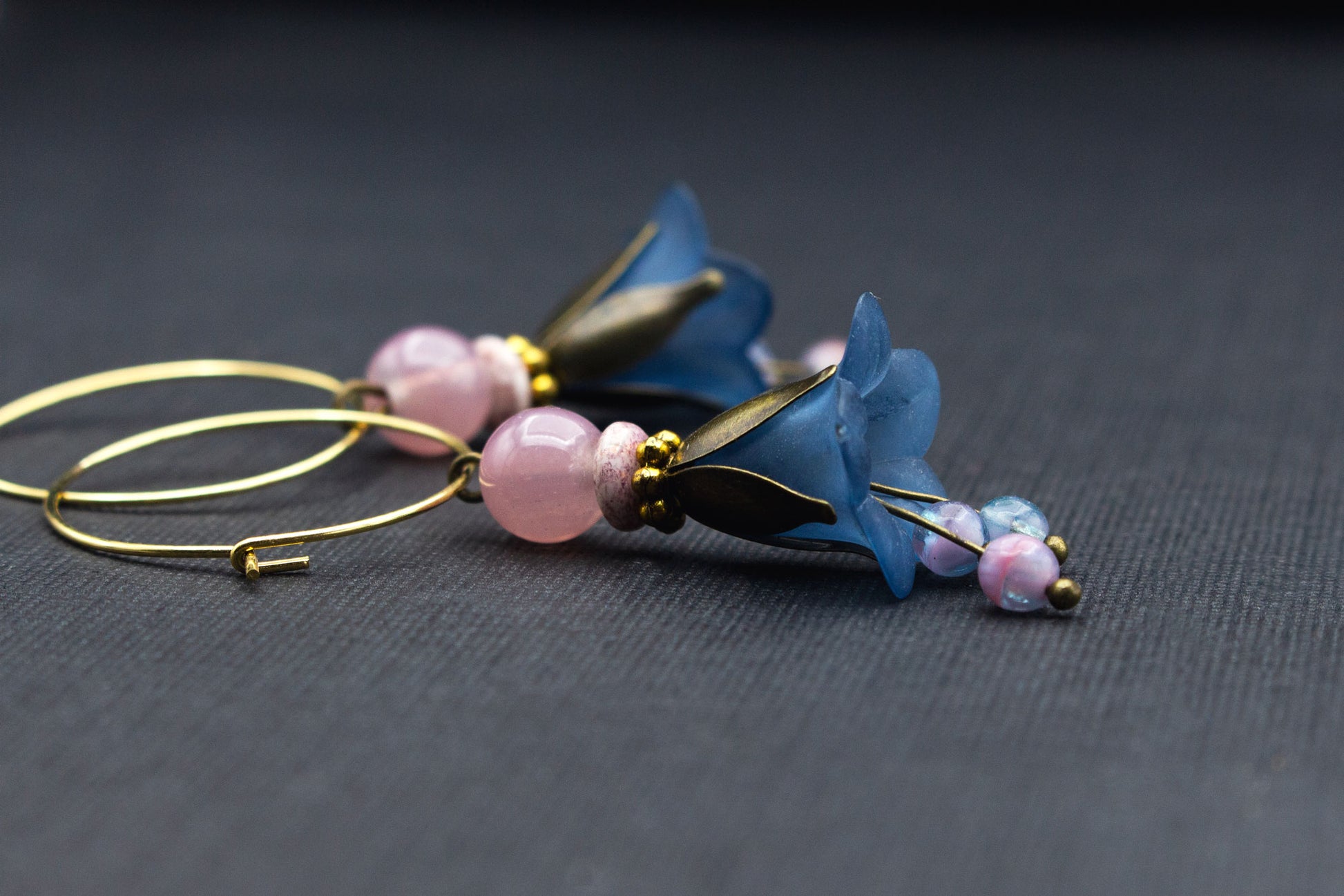Detailaufnahme goldfarbener Creolen mit Blüten in Rauchblau und rosa Glasperlen