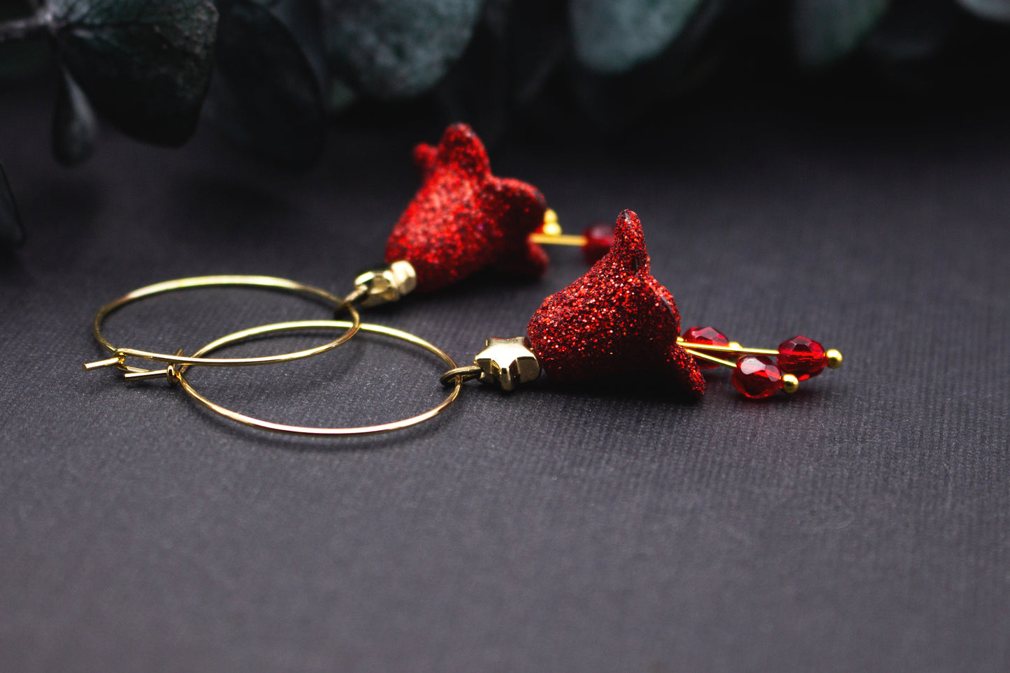 Detailansicht einer glitzernden roten Blüte an goldfarbener Creole mit kleinem Stern und roten Glasperlen, feine Material- und Lichtstruktur sichtbar