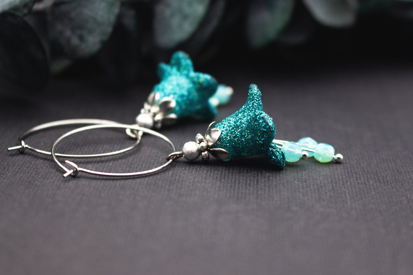 Detailansicht eines glitzernden Türkis-Anhängers an silberfarbenen Creolen, kombiniert mit milchigen Glasperlen und feinen Metallelementen