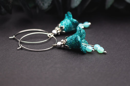 Creolen Ohrringe in Türkis mit glitzerndem Tropfenanhänger, milchigen Glasperlen und silberfarbenen Metallelementen, detailreiche Nahaufnahme